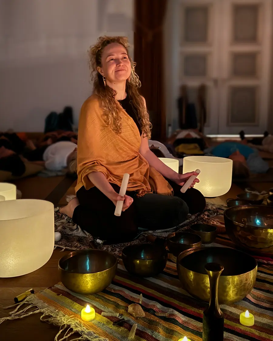 Anna Burger lächelnd zwischen Kristall- und tibetischen Klangschalen während eines Klangbads