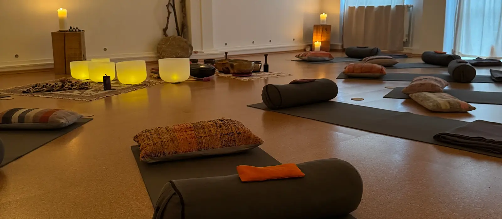 Eine Matte mit Bolster, Kissen und Decke im Innenraum, dahinter Kristallklangschalen